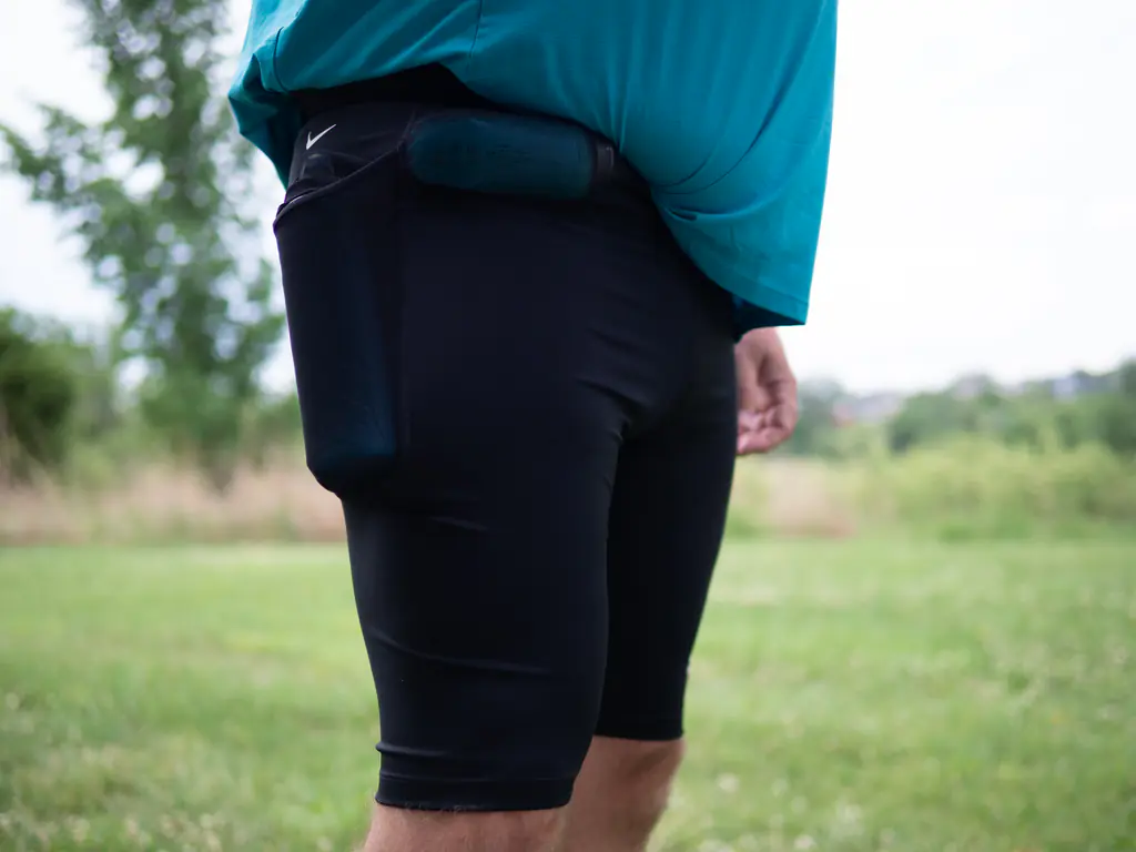 A runner wearing the half tights, with a 500ml soft flask in the side pocket and a 150ml nutrition flask in the front right waist pocket, shown from a front side angle A runner wearing the half tights, with a 500ml soft flask in the side pocket and a 150ml nutrition flask in the front right waist pocket, shown from a front side angle
