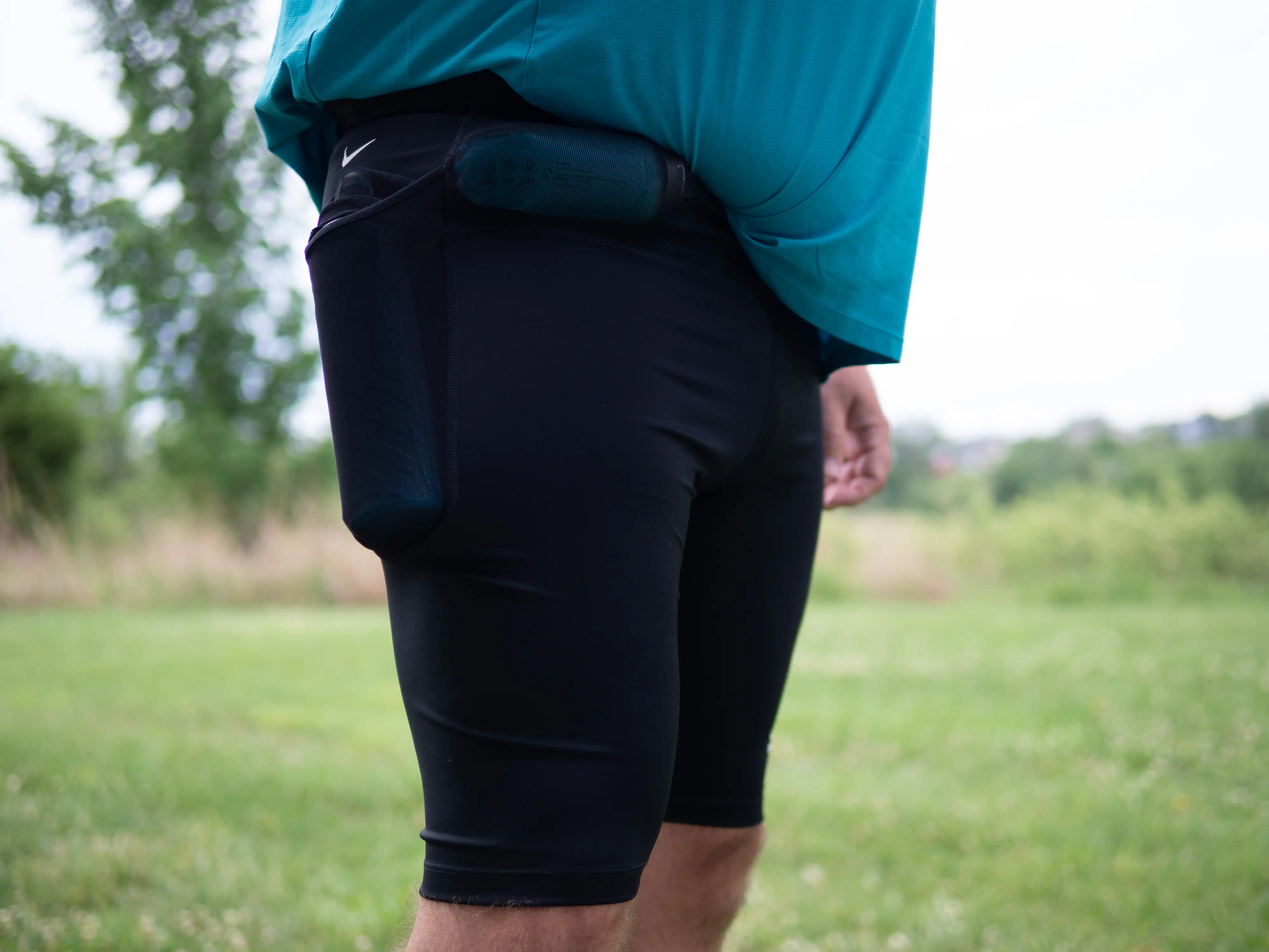 A runner wearing the half tights, with a 500ml soft flask in the side pocket and a 150ml nutrition flask in the front right waist pocket, shown from a front side angle