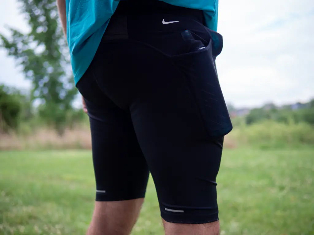A runner wearing the half tights, with a 500ml soft flask in the side pocket and a 150ml nutrition flask in the front right waist pocket, shown from a rear side angle A runner wearing the half tights, with a 500ml soft flask in the side pocket and a 150ml nutrition flask in the front right waist pocket, shown from a rear side angle
