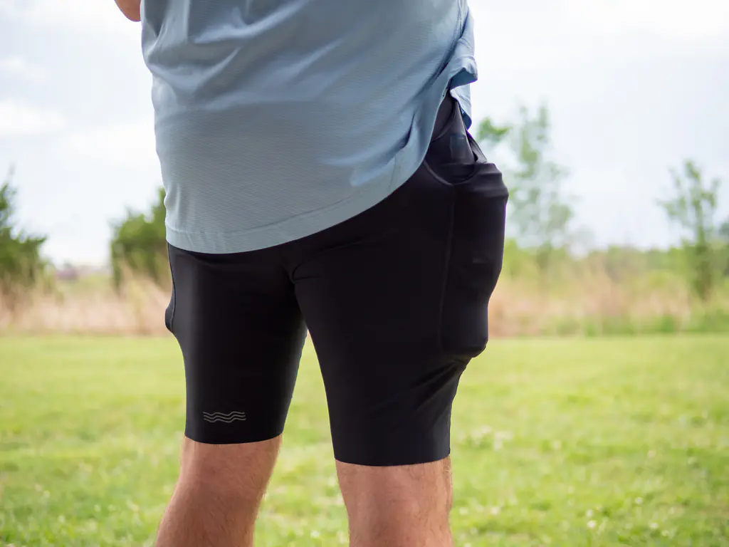A rear-side-view of a runner wearing the half tights, with the side pockets loaded with both a 500ml soft flask and a 150ml nutrition flask, which bulges quite a bit. A rear-side-view of a runner wearing the half tights, with the side pockets loaded with both a 500ml soft flask and a 150ml nutrition flask, which bulges quite a bit.